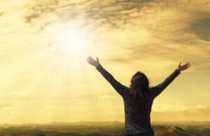silhouette of person with arms up in a victory pose, looking out over open spaces