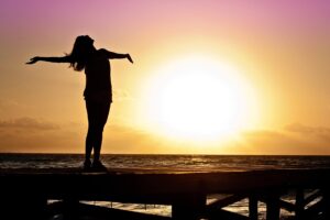 Woman standing on a dock with arms outstretched to the sun.